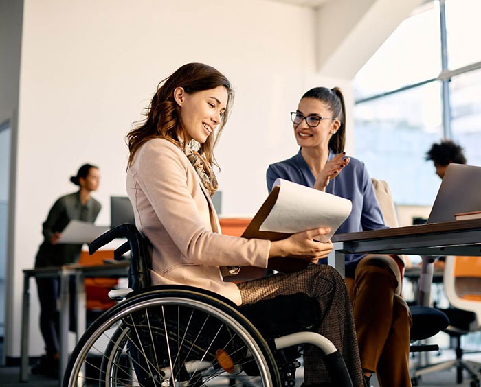 Woman in wheelchair assists a colleague with an accessibility test in an office.
