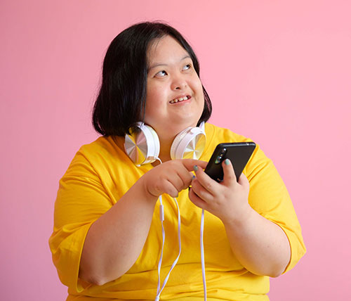Cheerful young woman with Down syndrome listens to music on a pink background.