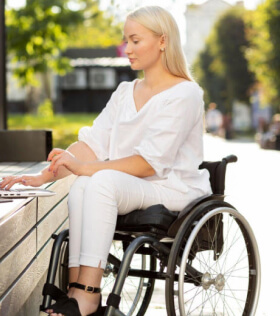 A woman seated in a wheelchair is working on her laptop.