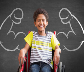 A smiling boy in a wheelchair with chalk superhero arms drawn behind him.