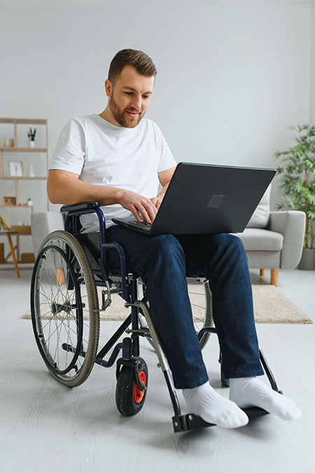 Man in wheelchair using laptop in a home environment.